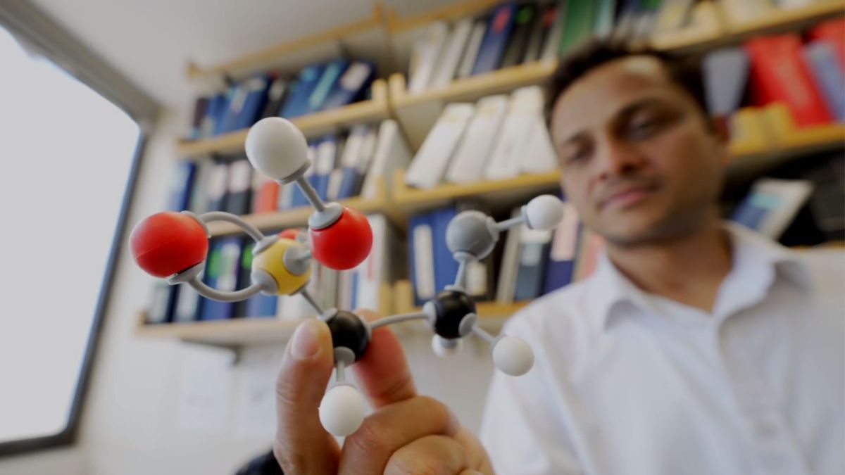 photo shows a man with tan skin and black hair wearing a white button down shirt and holding a molecular model of taurine, an atypical amino acid